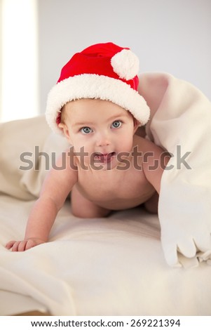 Baby crawling from under duvet wearing a santa hat