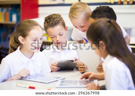 Happy students in classroom using a digital tablet, they are all wearing uniforms.