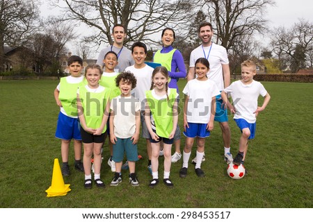 A group portrait of a kids soccer team, behind them are their coaches. They are all smiling and look happy.