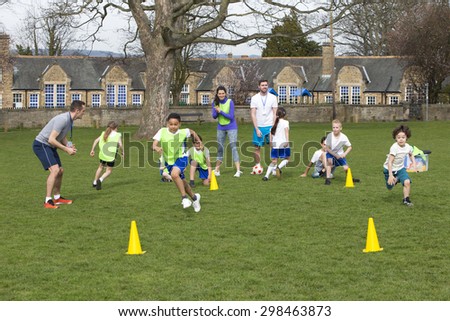 Adults on grassed area with school children supervising a football training session, Everyone can be seen running around cones. School building can be seen in the background.