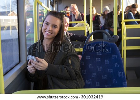 Young woman smiling for the camera on the bus with her smartphone in her hands.