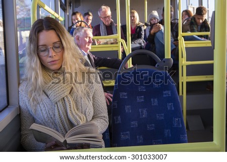 Woman sitting on the bus, reading her book with her spectacles on.