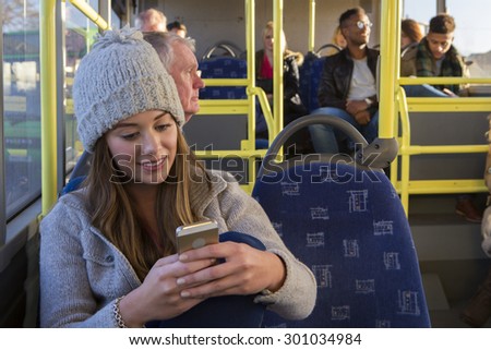 Young woman using her smartphone on the bus. There are other people sitting on the bus in the background.