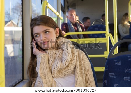 Teenager sitting on the bus. She is looking out the window and is on the phone to someone.