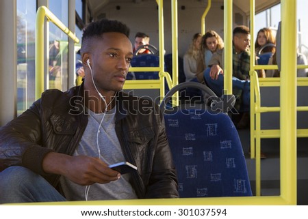 Attractive young man on the bus. He has earphones in which are attached to his smartphone.