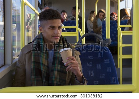 Attractive young man sitting on the bus with a cup of coffee. He is looking out the window and is smiling.