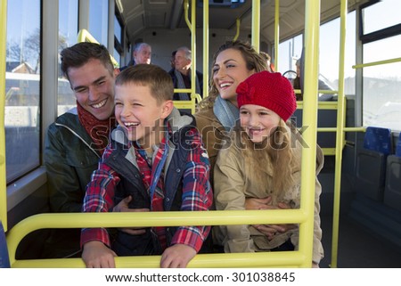 Happy family on the bus. The children are sitting on the knees of their parents and looking out the window. They are all laughing and smiling.