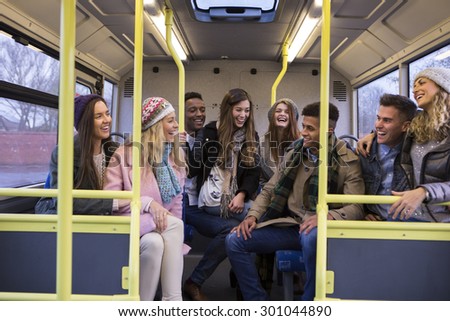 Group of young adults sitting together at the back of the bus. They are laughing and talking.