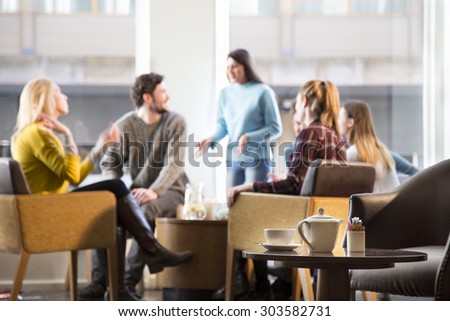 Group of friends in a cafe. They are all young adults and are talking in the background. A coffee set is in focus on a table in the foreground.