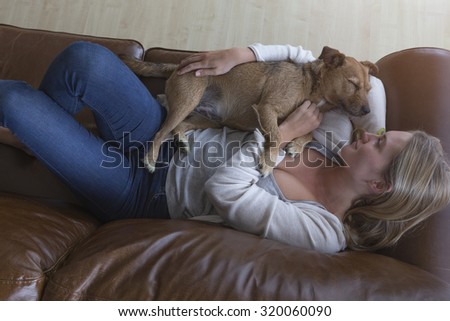 Ariel view of a woman cuddling her pet dog on a leather sofa.