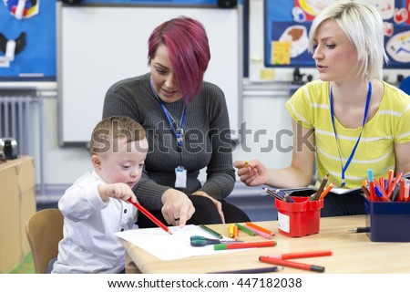 Nursery teacher sitting with a parent and her Down Syndrome son in the classroom. they are discussing the little boys progress.