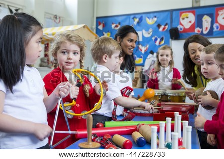 Nursery children playing with musical instruments in the classroom. One little girl is looking at the camera with a tambourine.