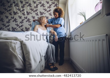 Home Caregiver helping a senior woman get dressed in her bedroom.