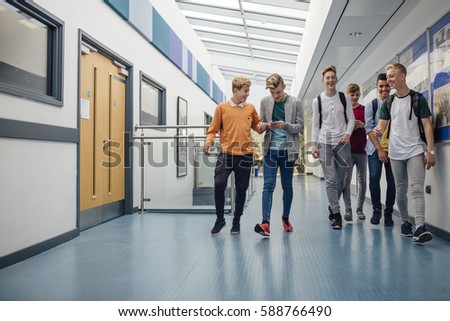 Group of teenage boys are walking down the school hall together to go for their lunch break. They are talking and laughing and some of the boys are using smart phones.