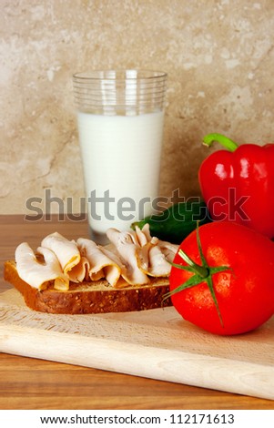 tasty sandwich on a wholewheat bread with a glass of milk and vegetables on a background