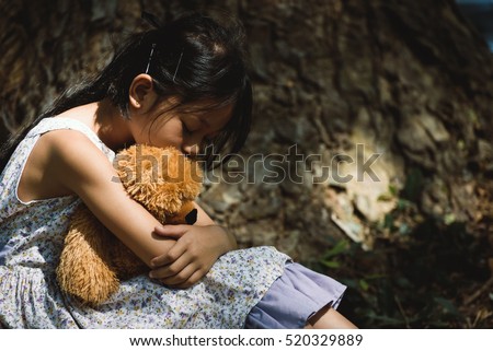 Adorable sad girl with teddy bear in park, Little girl is hugging a teddy bear.Upset child.