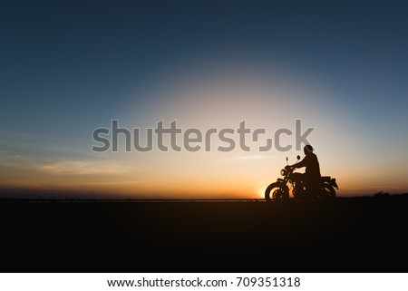 Silhouette of young man biker  and a motorcycle on the road with sunset light background