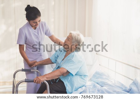 woman caregiver and elderly patient on examination couch. Happy nurse holding hand of senior to help senior patient. female nurse supporting senior disabled woman with walker at hospital. Health care