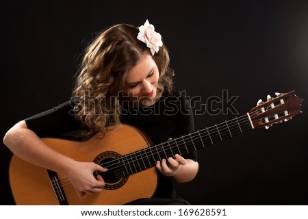Beautiful young female guitar player against black background