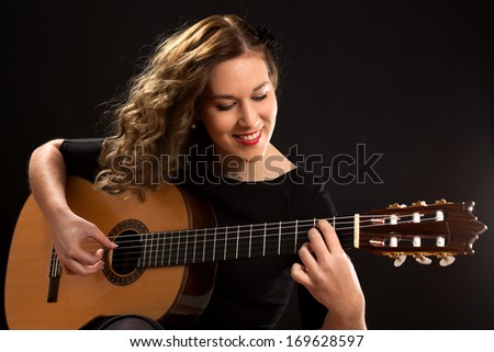 Beautiful young female guitar player against black background