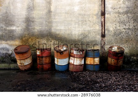 Abandoned rusty steel barrels in front of a grungy wall.