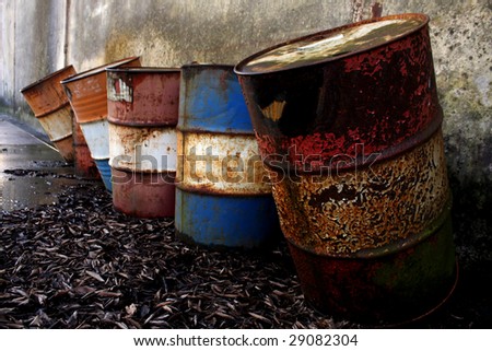 Abandoned rusty steel barrels on wet leaves in front of a grungy wall