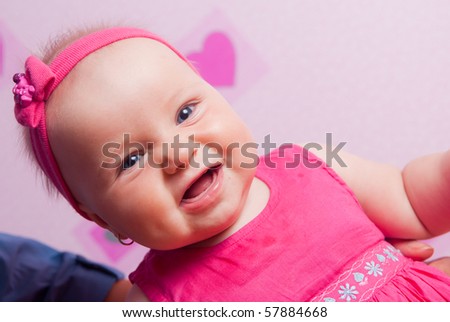 Smiling little baby girl sitting at the pink wall in pink headband and dress