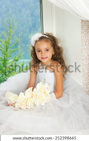 the elegant girl in a white ball dress sits on a window sill and watches a landscape a window