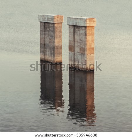 Bridge concrete pylons rise from the water. Sunset light. Abstract concept.