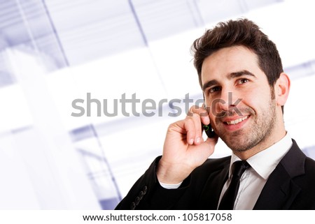 Young smiling businessman calling on phone at office