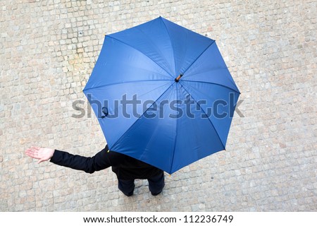 Business man hidden under umbrella and checking if it\'s raining