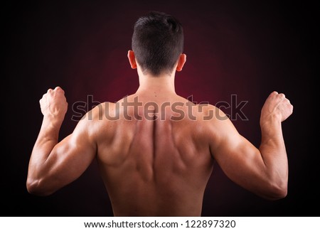Strong young man back on dark background