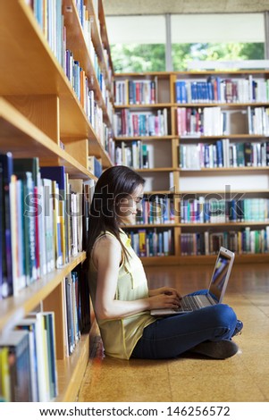 Young smiling student using her laptop in a library
