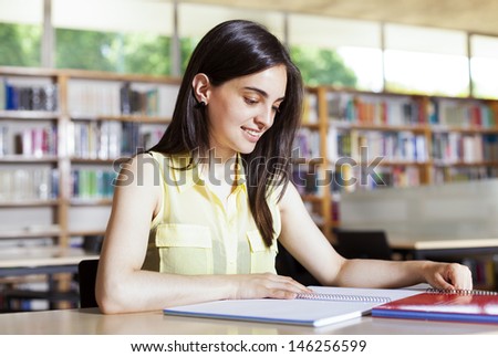 Portrait of a female student with open book reading it in college library