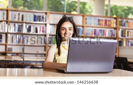 Smiling female student working with laptop in a high school library