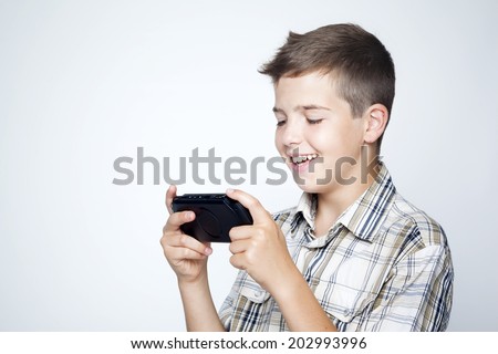 A teen boy playing video games in a portable game console against gray background