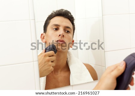 Young man shaving with electric shaver at the bathroom