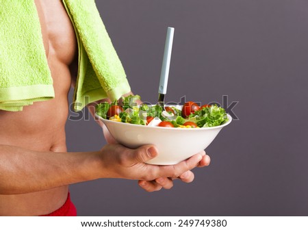 Fit man holding a bowl of fresh salad on grey background