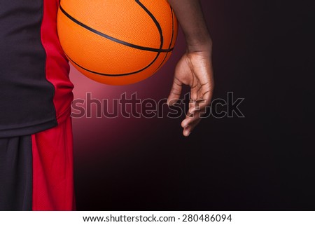 Rear view of a basketball player holding a basketball against dark background