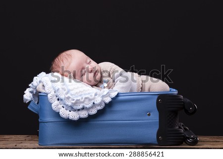 Newborn baby sleeping inside trolley bag against black background