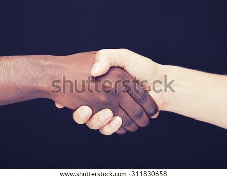 African and a caucasian man shaking hands over dark background