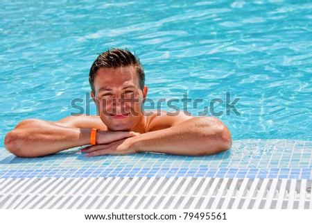Young wet tanned muscular man posing in the swimming pool