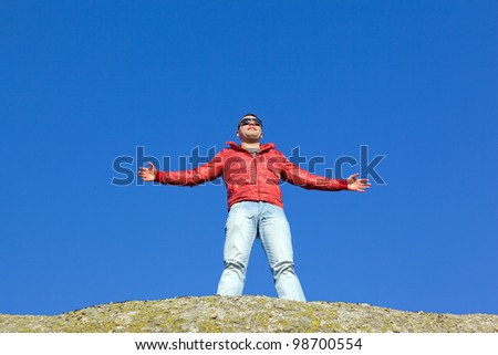 Handsome young man with arms wide open smiling against sky
