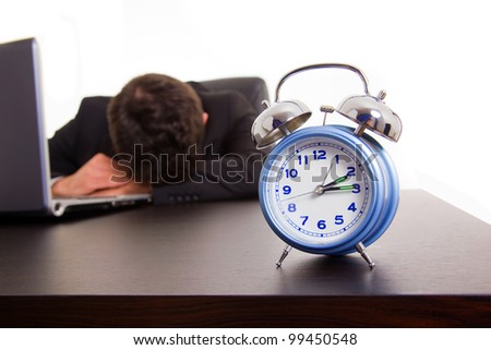 Exhausted young business man sleeping next to his laptop computer at the desk, isolated on white