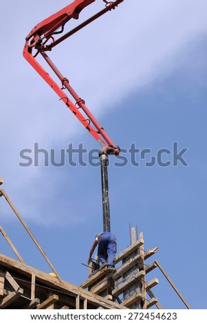 Builder worker with tube from truck mounted concrete pump pouring cement into formwork reinforcement