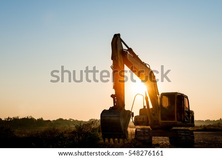 Track-type loader excavator machine doing earthmoving work at construction site on sunset background