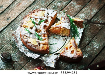 Pieces of apple pie sprinkled with powdered sugar. Top view. Homemade cut apple cake  decorated slices of lemon and green spruce branches on a wooden background. Food. Dessert. Rustic dark food style.