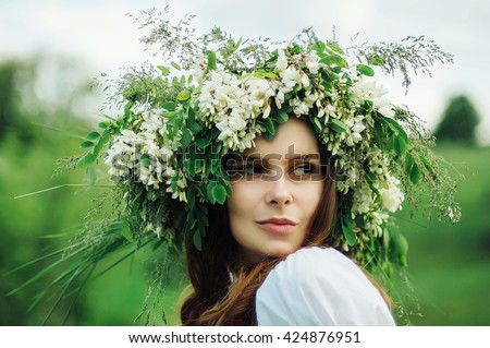 Young pagan Slavic girl conduct ceremony on Midsummer. Beauti girl dressed in a white blouse with embroidery, denim shorts, boots with grass Acacia wreath on his head against the background of nature