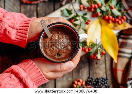 Woman holding cup of hot chocolate. Hot Chocolate in wooden table.  Woman having a cup of coffe. Rose hip tea and fresh rose hips.\
Autumn composition.
