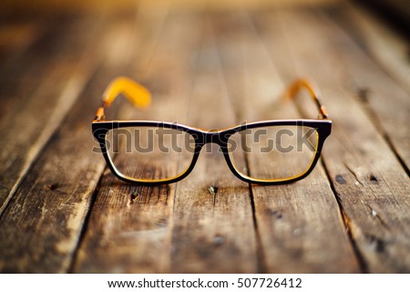 glasses  lie on the dark wooden table.   Black orange  glasses on wooden table. Office workplace with glasses on wood table. Glasses with orange rim. Orange Case for storage points.